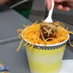 Skyline Chili Ice Cream with chili sauce, cheddar cheese, cinnamon, and cocoa powder on a wooden table.